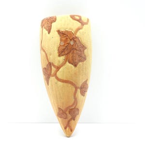 May include: A wall-mounted planter with a tapered, cone-like shape. The surface is a light beige color and features a carved, raised design of brown vines and leaves that wrap around the exterior of the ceramic vessel in a continuous pattern.