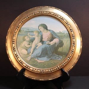 May include: A framed print of a painting depicting the Madonna and Child with Saint John the Baptist. The painting is set against a green and blue landscape. The frame is gold and ornate.