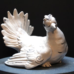 May include: White ceramic figurine of a bird with a long tail and black painted details. The bird is perched on a round base.