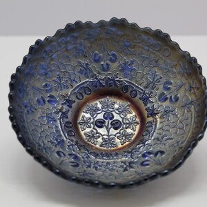 May include: A blue iridescent glass bowl with a scalloped edge and a floral design. The bowl has a center design of a flower with three leaves.