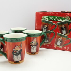 May include: Set of four ceramic mugs with a festive design. Each mug features a green handle and rim, with a red body and a painted image of a chef. The box reads "Tis The Season".