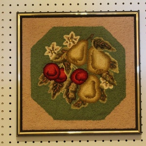 May include: A framed rug with a green background and a design of pears and red apples. The rug is surrounded by a gold frame.