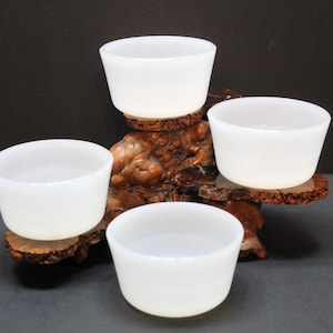 May include: Four white ceramic bowls are arranged on a wooden stand. The stand is carved with a natural wood design. The bowls are all the same size and shape.