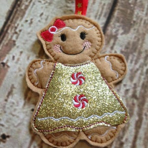 May include: A gingerbread person ornament with a gold glitter dress and red and white candy cane accents. The ornament has a red bow on its head and a smiling face.
