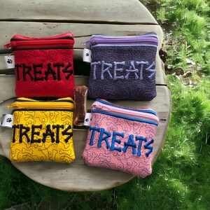 May include: Four small zippered pouches with a bone pattern and the word "TREATS" embroidered on each in different colours: red, yellow, purple, and pink.