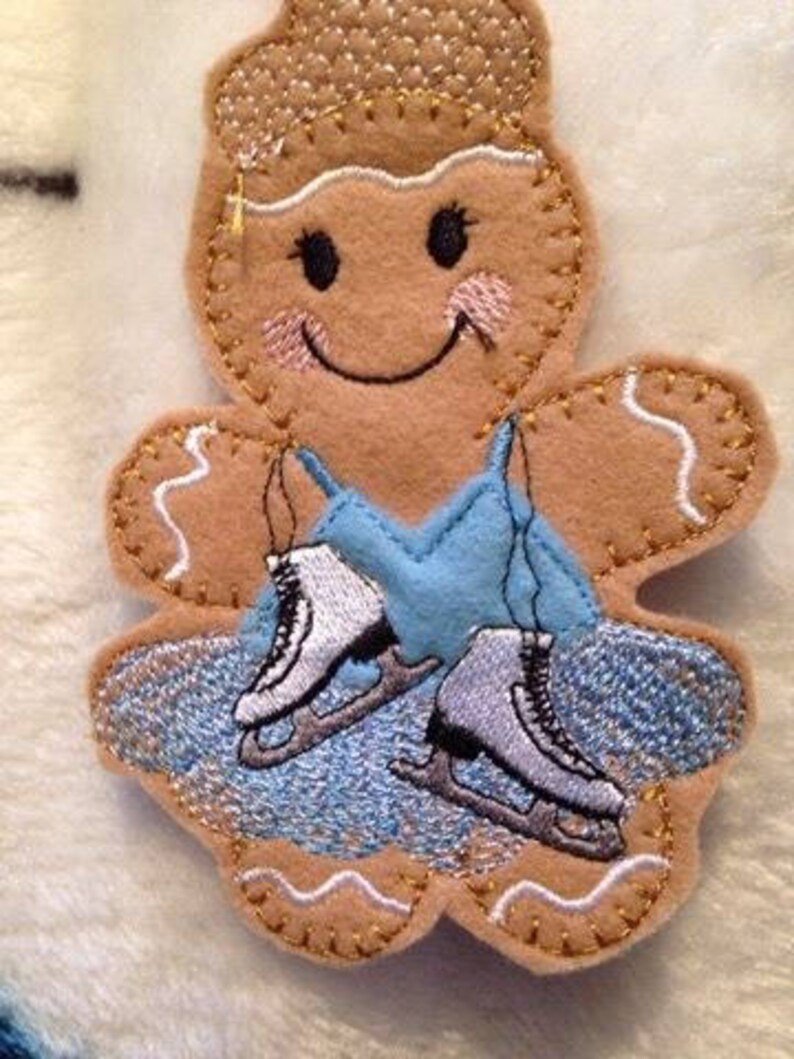 May include: A gingerbread person wearing a blue dress and ice skates. The gingerbread person has a smiling face with rosy cheeks and a gold crown.