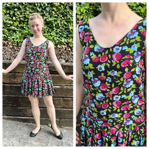 May include: A sleeveless black dress with a V-neckline and a pleated skirt. The dress is adorned with a vibrant floral pattern in shades of pink, blue, and green.