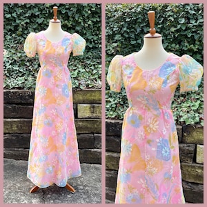 May include: A vintage-style, floor-length dress in pink with a floral pattern featuring yellow, blue, and white flowers. The dress has short, sheer, puffy sleeves and is displayed on a mannequin.