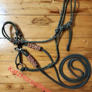 May include: A dark green and orange rope horse halter with a matching lead rope. The halter features orange and gray braided accents and gold-colored metal hardware. The text "Katz HorseWear" is visible in the image.
