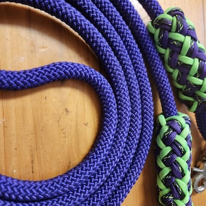 May include: A purple rope dog leash with two green and purple knotted handles. The leash has a metal clip on one end.
