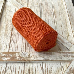 May include: A roll of orange burlap ribbon. The ribbon is made of a coarse, woven fabric and has a rustic look.