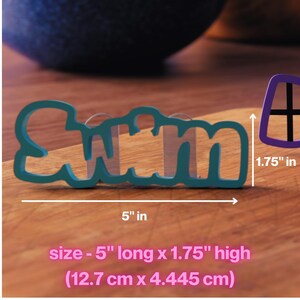 Op de afbeelding: Blauwe plastic koekjesvormer in de vorm van het woord "Swim" met een lengte van 12,7 cm en een hoogte van 4,45 cm.