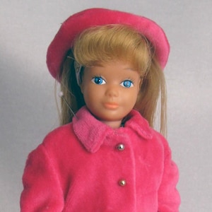 May include: A pink doll with blonde hair wearing a pink coat and hat, white gloves, and pink shoes. The doll is holding a pink purse with a gold chain.