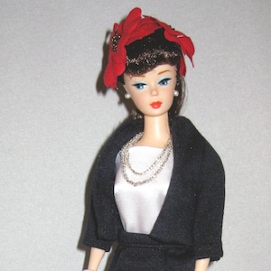 May include: A doll wearing a black dress and jacket with a white blouse, red flower hat, and black heels. The doll is holding a blue and white gingham shirt.
