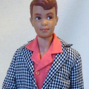 May include: A doll with auburn hair wearing a coral-colored collared shirt and a black and white houndstooth patterned blazer. The doll has a neutral expression and is facing forward.