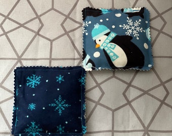 Könnte beinhalten: Zwei blaue Stoffquadrate mit weißen Schneeflocken und einem Pinguin-Design. Der Pinguin trägt einen blau-weißen Hut und einen Schal.