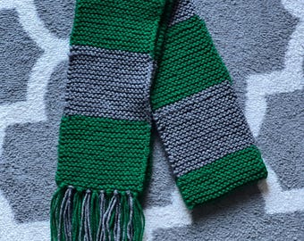 Könnte beinhalten: Ein gestrickter Schal in Grün und Grau mit Fransen an den Enden.