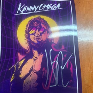 May include: A rectangular print featuring a stylized illustration of Kenny Omega wearing sunglasses, set against a purple grid background with a yellow sun. The name KENNY OMEGA is printed at the top, and a silver ink signature is visible on the right.