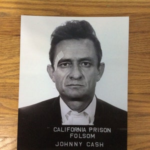 May include: Black and white mugshot of Johnny Cash with the text "California Prison Folsom Johnny Cash" at the bottom.
