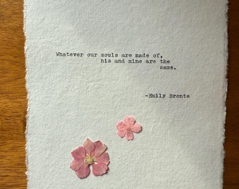 Könnte beinhalten: Ein strukturiertes weißes Papier mit dem Zitat "Whatever our souls are made of, his and mine are the same." von Emily Brontë. Zwei getrocknete rosa Blüten sind auf dem Papier befestigt, was dem Kunstwerk eine zarte Note verleiht.