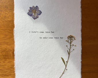 Könnte beinhalten: Weißes strukturiertes Papier mit einer gepressten lila Blume und einem getrockneten Zweig. Der Text "I didn't come this far to only come this far" ist mit schwarzer Tinte gedruckt.