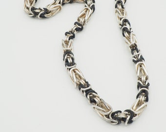Puede incluir: Un collar de cadena plateado y negro con un diseño de estilo bizantino.