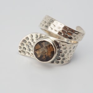 May include: A silver ring with a hammered texture and a brown gemstone. The ring is designed to wrap around the finger.