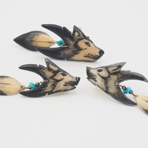 May include: Three carved bone wolf head pendants with turquoise beads and feathers. The pendants are black and white with intricate details.