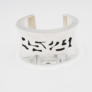 May include: Silver cuff bracelet with a cutout design featuring abstract shapes in black.