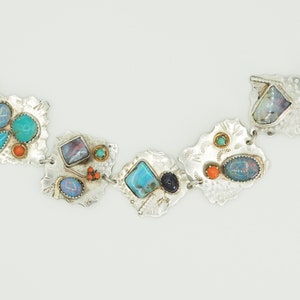 May include: A silver bracelet with a geometric design features a variety of colorful stones, including turquoise, opal, and coral.