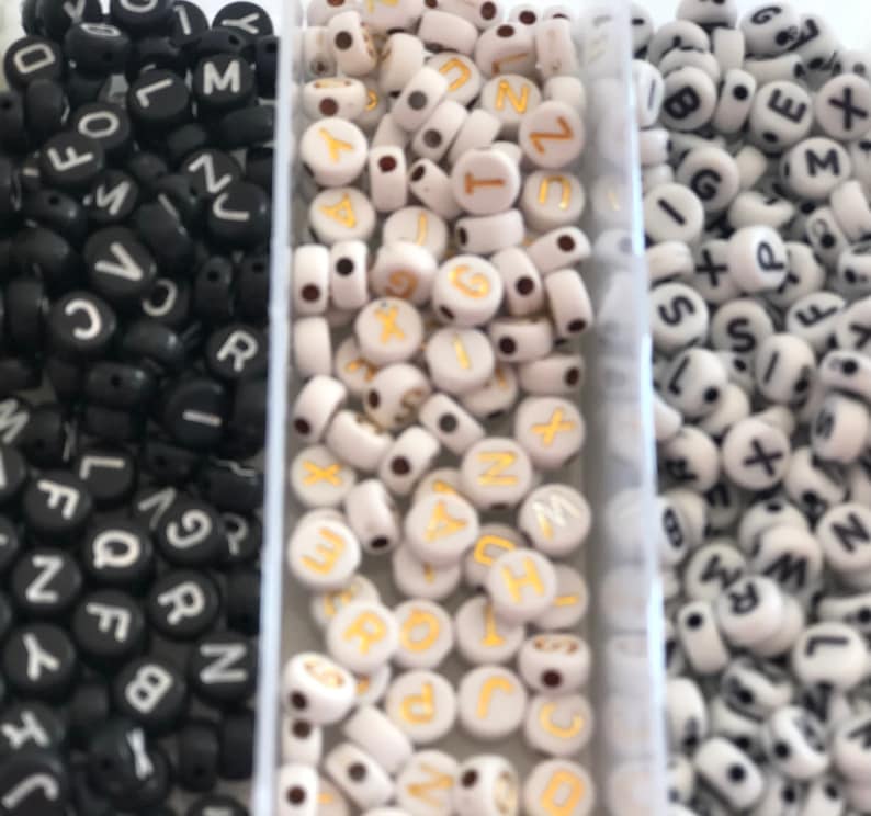 Op de afbeelding: Drie bakjes met letter kralen. Het eerste bakje heeft zwarte kralen met witte letters. Het tweede bakje heeft witte kralen met gouden letters. Het derde bakje heeft witte kralen met zwarte letters.