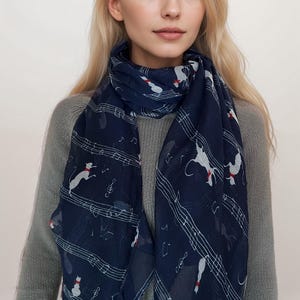 May include: A navy blue scarf with a white musical note and cat design. The scarf is made of a lightweight fabric and is perfect for adding a touch of style to any outfit.