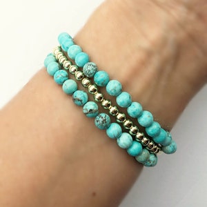 Op de afbeelding: Drie turquoise kralen armbanden met gouden kralen ertussen. De armbanden zijn gestapeld op de pols van een persoon.