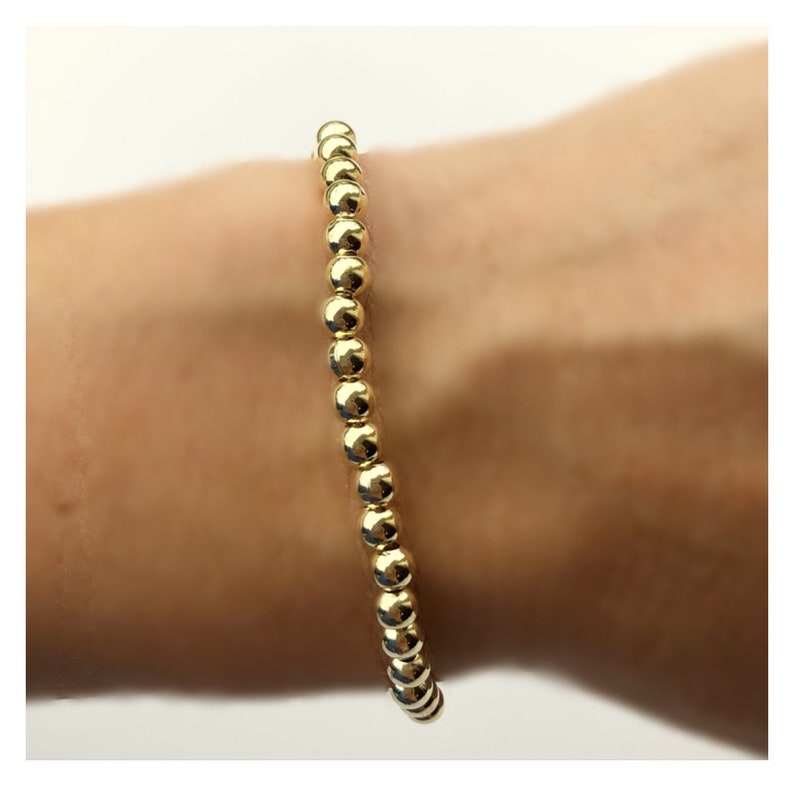 Op de afbeelding: Een gouden kralen armband met een eenvoudig ontwerp. De armband is gemaakt van kleine, ronde kralen die aan elkaar geregen zijn op een dunne ketting.