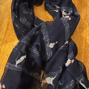May include: A navy blue sheer scarf with a white musical note and white cat design. The cat has a red bow on its neck.