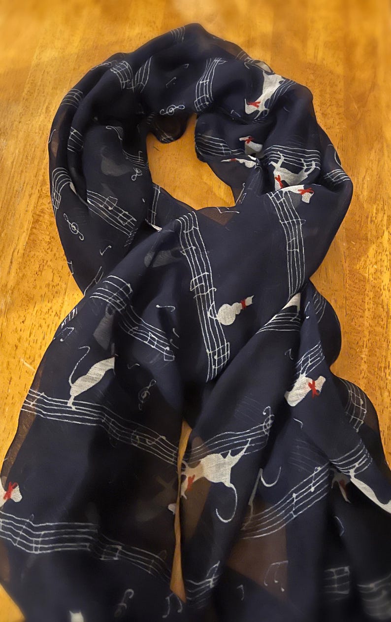 May include: A navy blue sheer scarf with a white musical note and white cat design. The cat has a red bow on its neck.