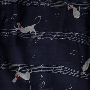 May include: A navy blue scarf with a white musical note pattern and white silhouettes of cats wearing red bows. The scarf is made of a sheer fabric.