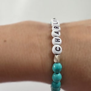 Op de afbeelding: Een turquoise en witte kralen armband met de naam "CHARLIE" gespeld in witte kralen.