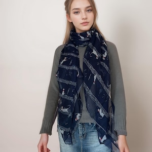 May include: A woman wearing a gray sweater and a blue scarf with a musical note and cat print. She is also wearing a denim skirt.