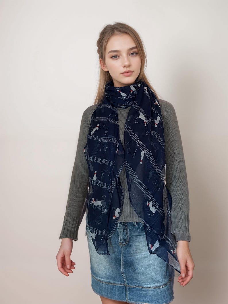 May include: A woman wearing a gray sweater and a blue scarf with a musical note and cat print. She is also wearing a denim skirt.