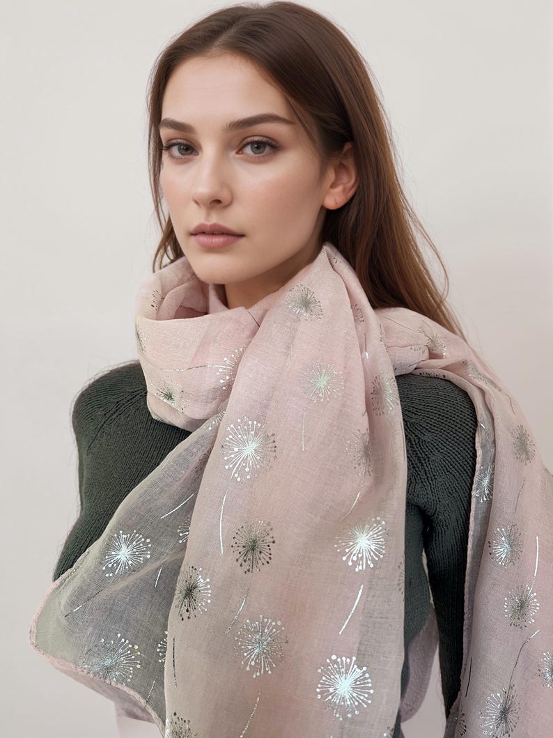May include: A pink scarf with a silver dandelion print. The scarf is made of a soft, lightweight fabric and is perfect for adding a touch of elegance to any outfit.