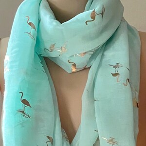 May include: A light blue scarf with a gold flamingo print. The scarf is made of a soft, sheer fabric and is perfect for adding a touch of whimsy to any outfit.