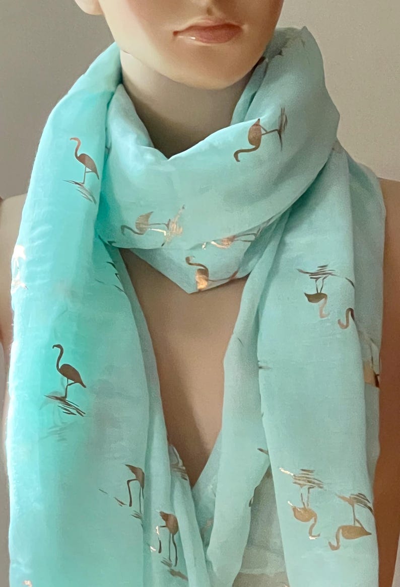 May include: A light blue scarf with a gold flamingo print. The scarf is made of a soft, sheer fabric and is perfect for adding a touch of whimsy to any outfit.