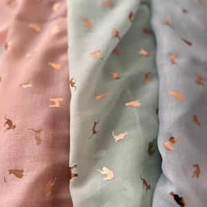 May include: Three scarves with a repeating pattern of gold metallic cats on a light pink, light blue, and blue background.