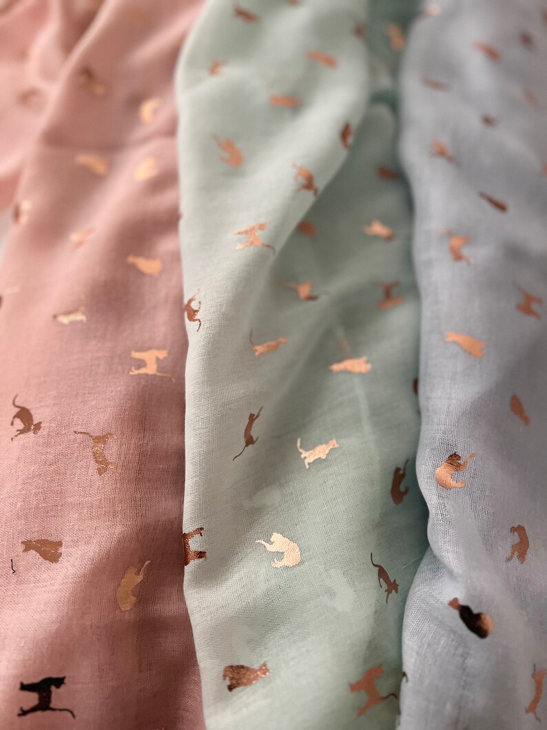 May include: Three scarves with a repeating pattern of gold metallic cats on a light pink, light blue, and blue background.