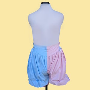 May include: A pair of split-color shorts featuring a light blue left side and a light pink right side. The shorts have a high-waisted design with a fitted waistband, gathered fabric creating a voluminous silhouette, and side ties for adjustment.