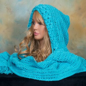 May include: A bright turquoise hooded scarf featuring a chunky crochet knit pattern with a cable-knit design along the hood edge and fringe detailing on the ends. The accessory is draped over a mannequin head with long blonde hair.
