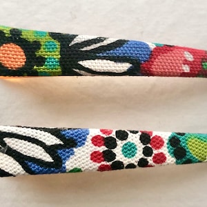 May include: Two colorful fabric hair clips with floral and geometric patterns. The top clip has a green, black, orange, and red design. The bottom clip has a white, black, blue, red, and green design.
