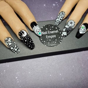 May include: Black and white nail art designs on long, almond-shaped nails. The designs include a crescent moon, stars, a spooky eye, and the words "Good Bye".