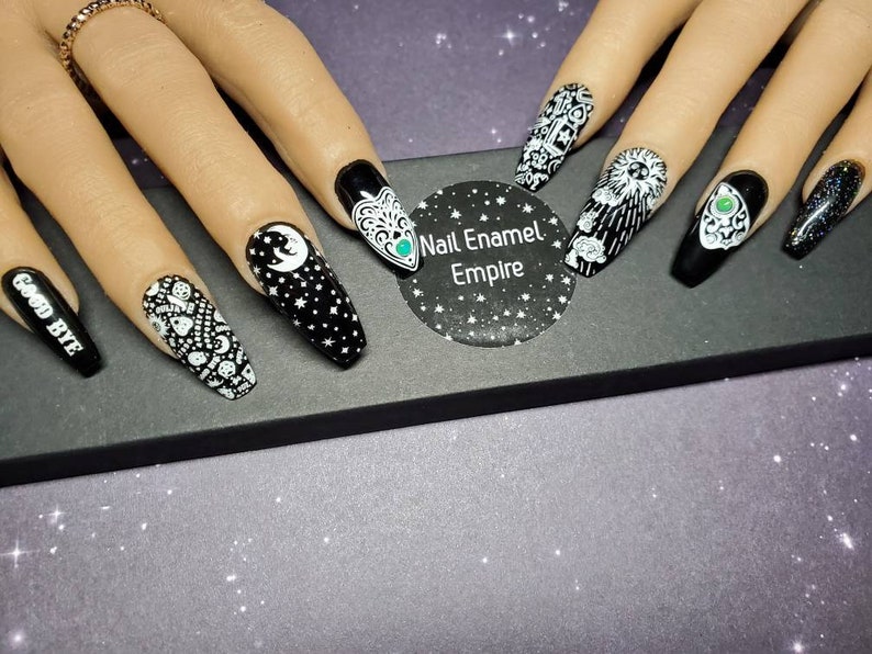 May include: Black and white nail art designs on long, almond-shaped nails. The designs include a crescent moon, stars, a spooky eye, and the words "Good Bye".